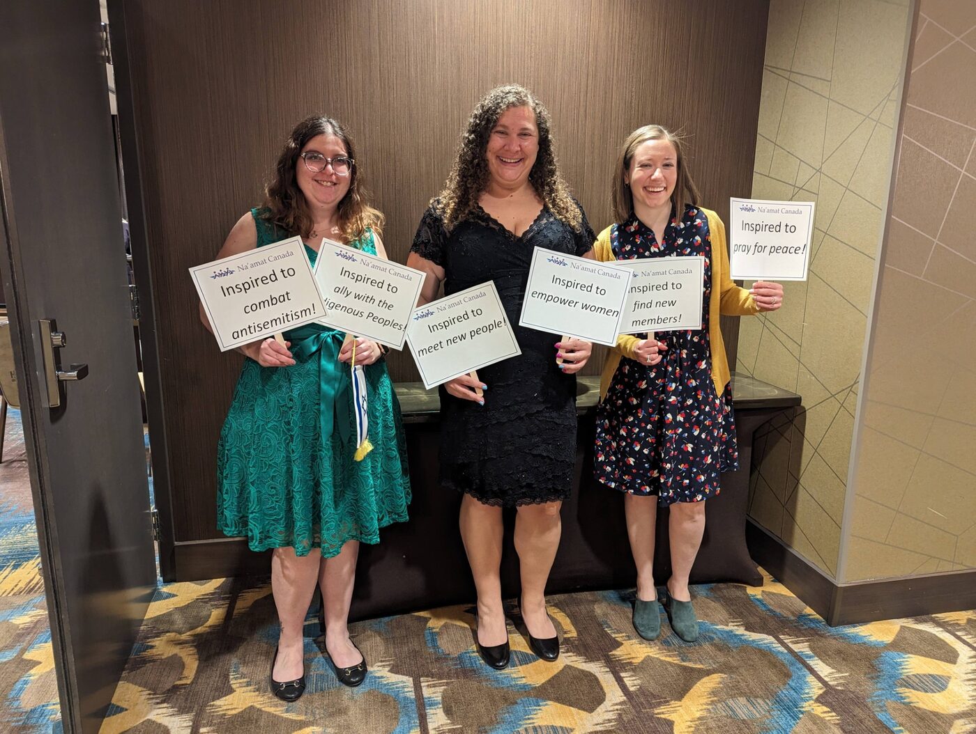 Na'amat Canada members holding signs reading “Inspired to combat antisemitism”, “Inspired to empower women” and “Inspired to pray for peace”